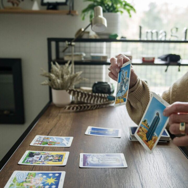 A person shuffles tarot cards on a wooden table indoors.