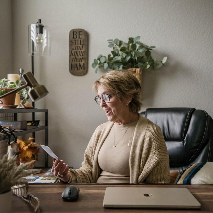 Woman working at a desk with plants and books in a cozy home office.