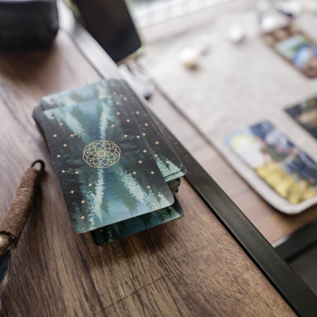 A tarot card deck sits on a wooden table with scattered white stones.