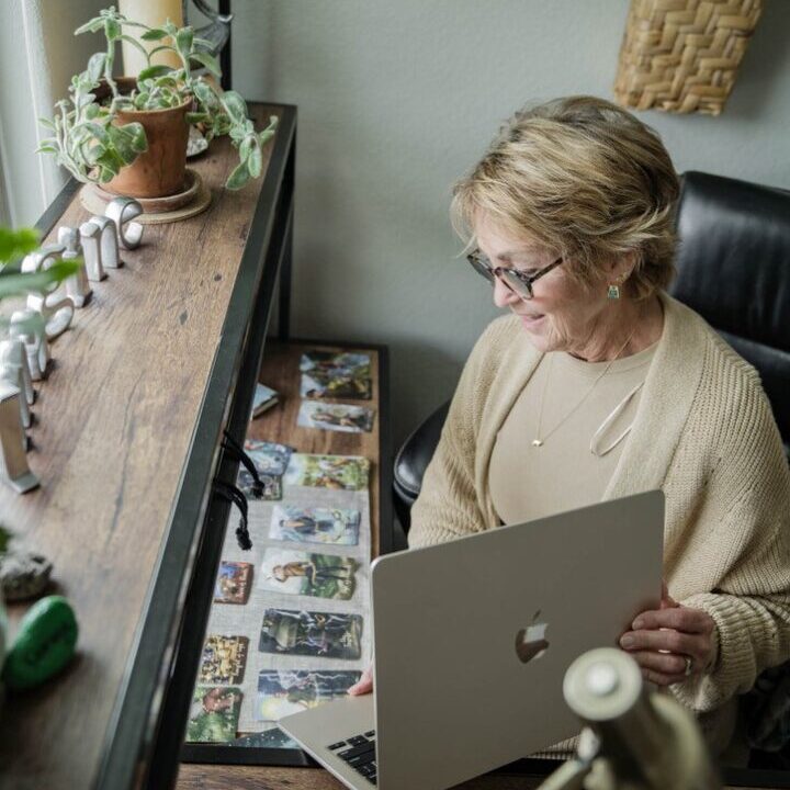 Woman working on a laptop while sitting by a window with plants.